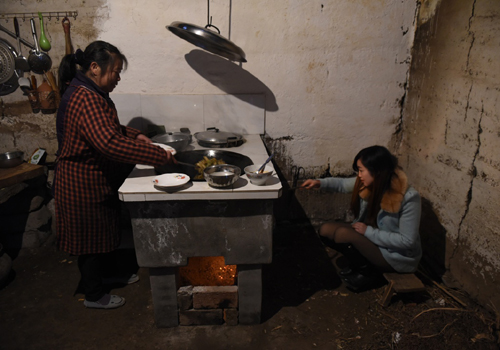 2月8日，在外打工归家的水井村曾家小妹（右）在帮母亲生火做饭。新华社记者 刘坤 摄