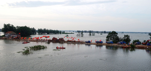 7月20日，考田河堤坝溃口成功合龙后，武警水电官兵挥舞旗帜庆祝。