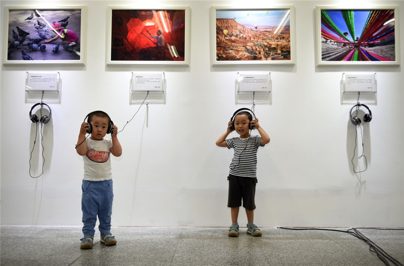 两名小朋友在北京京港地铁四号线国家图书馆站M地铁·影廊首期主题活动上聆听与展出照片内容相关的音乐