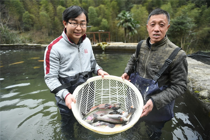 李爱平（左）与曾经的贫困户钟万银在展示他们养殖的虹鳟鱼