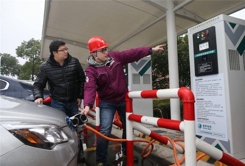 1月5日，在上海市顾戴路一处新能源汽车停车场，国网上海市南供电公司的工作人员（右）在指导市民使用充电桩。