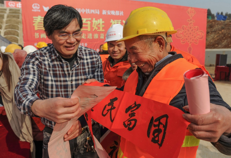 1月10日，在淮萧客车联络线工程安徽萧县古尚村段建设工地，中国书法家协会会员董正夫向即将返乡的农民工尹显坤（右一）赠送春联。
