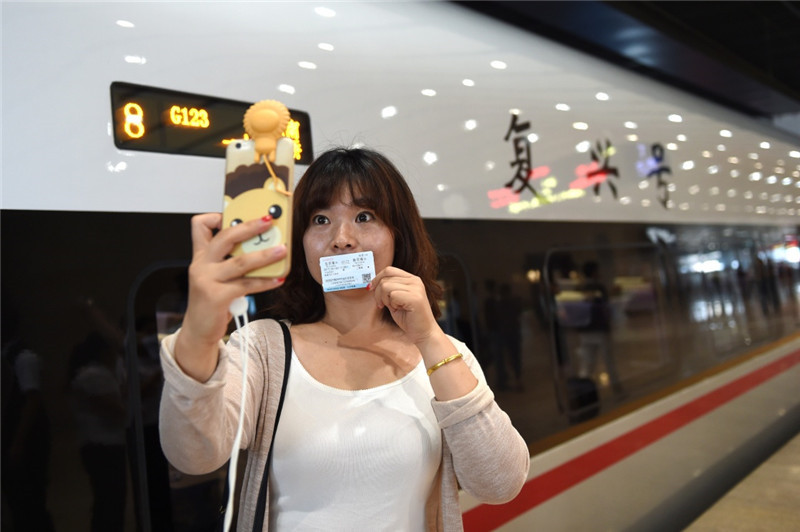 6月26日，在北京南站，一位乘坐“复兴号”G123次列车的乘客在车外与列车合影。
