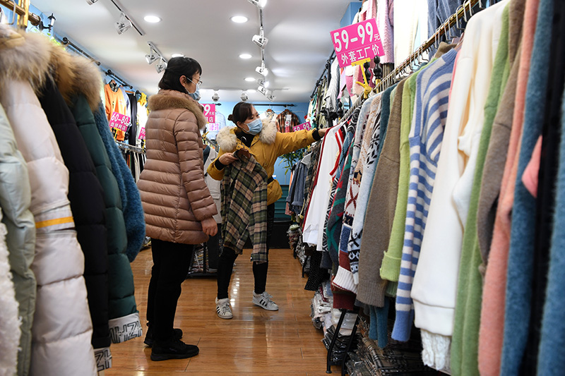 3月6日,在綦江区的一家服装店内,店主在向顾客推荐服饰.