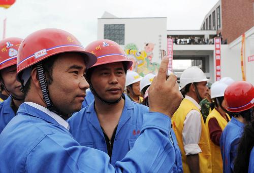 5月9日,江苏援建工人在竣工仪式上用手机留影。当日,江苏援建四川绵竹市的第一批49个项目在地震灾区绵竹市孝德镇举行竣工仪式。这批项目包括学校、医院等公共设施。 新华社记者 杨磊 摄