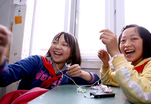 2009年4月30日,杨芹(左)在课间休息时和同学一边听音乐,一边叠纸鹤。脸上、身上满是灰尘,一双水汪汪的大眼睛怯生生地望着——2008年5月13日上午9时,在四川省绵竹市汉旺镇武都小学的废墟中,10岁的杨芹在等待救援。为了防止碎石砸伤她的头部,救援人员给她戴上了一顶红色的安全帽。那时起,杨芹就有了个昵称——“小红帽”。那顶在灰色废墟中格外显眼的“小红帽”,代表着生的希望与活下去的动力。经历了近20个小时的漫长等待,“小红帽”终于被德阳消防支队的救援人员从废墟中抱出。然而就在杨芹所在班上,70多个孩子只有一半活了下来。 “5·12”大地震已经过去快一年的时间,现在的“小红帽”还好吗?带着思念与牵挂,记者驱车前往汉旺镇的板房学校,探望在地震中生还的幸运儿——“小红帽”杨芹。从一群正在教室外的台阶上写英语作业的孩子中,我们找到了杨芹。见到记者来,杨芹站起身,脚步蹒跚地走了过来,显得有些羞涩。由于被埋时间过长,杨芹的右腿坏死感染,做了高位截肢手术,现在已经安装了假肢。“小红帽”特别喜欢笑,同学逗她,她马上咯咯地乐起来,很快就恢复了开朗的本性。为了尽快摆脱地震带来的阴影,现在的杨芹每周都