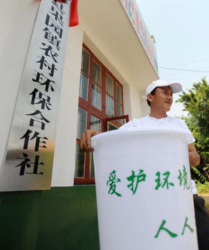 6月5日,长沙县果园镇农村环保合作社保洁员陈又专拿起保洁桶准备开始一天的工作。6月3日,一个市场化运营、致力于农村生活垃圾分类处理机制建设的农村环保合作社在湖南省长沙县果园镇成立。果园镇农村环保合作社按照“分户收集、分类减量、村民自治、政府补贴、合作社运作”的机制,在全镇每户建立小型垃圾池,并在每个村招募保洁员上门收购垃圾,农户只需每月交纳5元保洁费便可享受到上门分类回收垃圾的“环保服务”。保洁员通过分类收集处理,将可降解垃圾在垃圾堆沤池填埋处理,将不可降解的可利用垃圾送至废品公司,不可降解有害垃圾集中送至镇压缩中转站,然后统一运送到固体废弃物填埋场集中填埋。通过这种方法,在农村生活垃圾中只剩下10%左右的不可利用垃圾被送到县里的垃圾场进行填埋,极大地节约了土地资源和垃圾处理成本,同时为农户们带来了一个更加清洁健康的生产生活环境。 新华社记者 李尕 摄