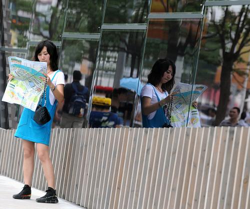 7月10日,一名游客在世博园内查看地图,她的身影映在展馆的玻璃墙上。新华社记者 燕雁 摄