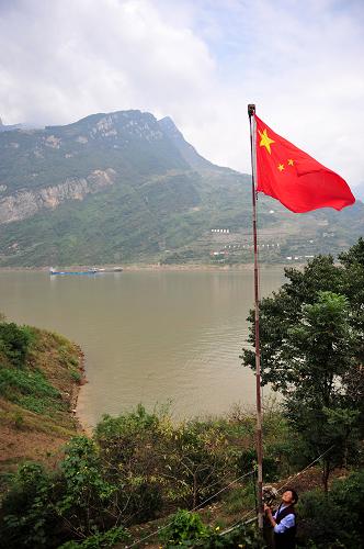 9月29日早晨,三峡移民颜道英在自家门前升起五星红旗。湖北省秭归县西陵峡村四组移民颜道英家门前,总有一面鲜艳的五星红旗迎风招展,颜道英一家是就地后靠移民,迁居后一家人的生活条件有了明显改善。2004年开始,她老伴,20几年的老村干部高秉钳就天天带着自己的儿孙在家门口举行“升旗仪式”,表达对祖国的热爱,直到2008年辞世。老伴去世后,颜道英接过老伴留下来的五星红旗,在旭日东升的早晨,她做的第一件事就是升旗,既表达感恩,也寄托思念。新华社发(郑家裕 摄)