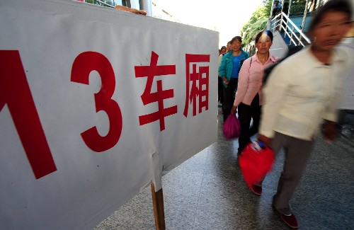 8月25日,在兰州火车站,乘坐“棉农专列”赴新疆摘棉的棉农从车站引导牌旁走过。