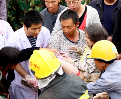 5月13日,救护人员把被救出的学生抬往医院。 四川绵竹市汉旺镇武都小学的教学楼在地震中倒塌,众多师生被埋在倒塌的校舍中。救援行动正在积极展开。 新华社记者 陈建力 摄