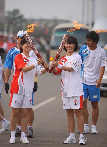 6月5日,火炬手刘娜(右二)与下一棒火炬手陈晓春交接后将两支火炬摆成英文字母“V”字形状。当日,北京奥运圣火在湖南湘潭传递。 新华社记者 邢广利 摄