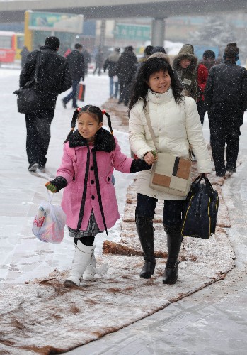 1月27日,一对即将检票进站的母女从兰州火车站站前广场铺设的防滑毯上走过。 新华社记者 韩传号 摄