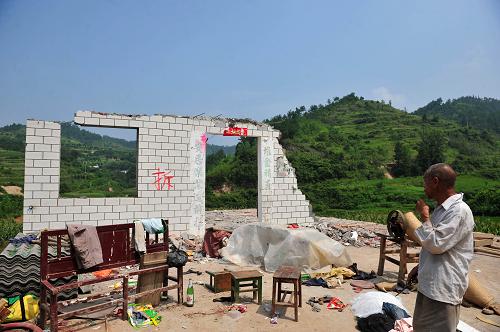 8月9日,湖北省郧县柳陂镇辽瓦村一位老人站在自家即将拆迁完毕的房子前。新华社记者 郝同前 摄