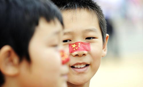 10月1日,来自河南的肖扬(左)和薛博文在脸上彩绘国旗图案,庆祝中国国家馆日。当日,上海世博会迎来中国国家馆日。新华社记者王建华摄
