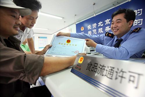 9月17日,个体工商户余明(左)从北京市工商局西城分局新街口工商所工作人员手中领到食品流通许可证。当日,北京市西城区首批个体工商户领到了食品流通许可证。根据国家工商总局《食品流通许可证管理办法》,从9月1日起,北京市工商局正式启动食品流通许可工作,对全市范围内的商场、超市、市场、食杂店以及影剧院、加油站、报刊亭等从事批发或零售预包装食品、散装食品的经营企业和个人实施食品流通许可。为做好许可证的受理、发放工作,北京市各级工商部门均在服务大厅设立了专门窗口,为申请人提供高效、便捷、优质的服务。新华社记者 张旭 摄