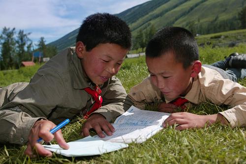 这是新疆布尔津县禾木哈纳斯乡哈纳斯村蒙古小学的两名学生在户外温习功课(2005年6月23日摄)。这所小学有近百名学生,其中大部分是蒙古族。禾木哈纳斯乡位于美丽的喀纳斯湖畔,近2000名蒙古族图瓦人生活在这里。新华社记者 沙达提 摄