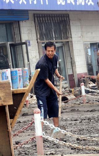 7月31日,一位居民在清理家门前的淤泥。洪灾过后,吉林省永吉县开始重建工作。由于受灾严重,很多居民家中留下大量淤泥,清理工作十分困难。居民们在依靠政府救援的同时,也积极开始自救,纷纷回到家中整理物品,找饮用水源、清理淤泥。新华社记者 宗巍 摄