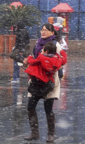 1月18日,一位旅客抱着孩子顶着风雪在铁路上海站广场进站候车。 当日,上海迎来降雪。上海铁路春运将于19日正式启动,铁路部门已采取开启地下临时候车点等措施应对风雪天气。新华社发
