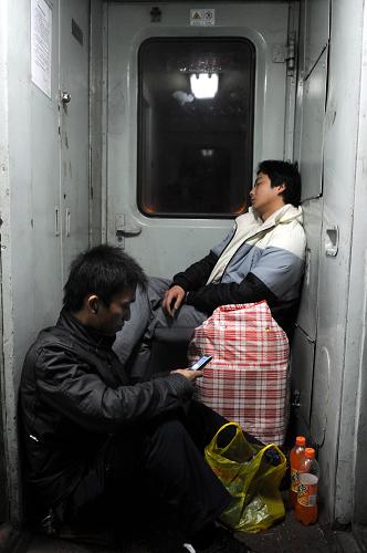 L160次列车上,两位没有座位的乘客在车厢连接处“栖身”(1月20日摄)。新华社记者 郭晨 摄