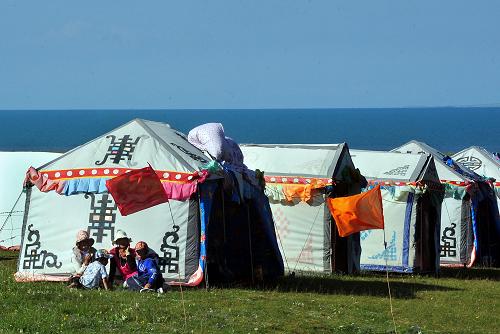 浪漫青海湖 几位牧民在青海湖畔的帐篷旅馆外等候游客(7月20日摄)。 入夏时节,青海湖的景色格外迷人。湖畔山清水秀,沿湖的草原像绿色的绒毯苍茫无际,鲜花竞放,菜花泛金,碧波万顷的湖水,像一面巨大的蓝色宝镜,在阳光下熠熠生辉。游客们置身于山、湖、花、草以及民俗风情相互衬映的绮丽景色之中,无不心旷神怡,引发联翩的浪漫遐想。 新华社记者 王颂 摄