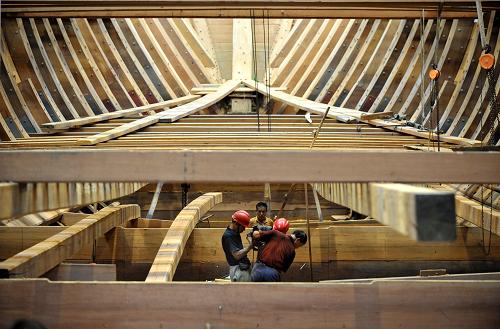 7月3日,明代宝船厂遗址上的复建厂房内,工人们在进行宝船木构件安装作业。 近日,南京“郑和宝船”复建工程取得重要进展。在位于明代宝船厂遗址上的复建厂房内,庞大的宝船主船体结构基本建成,即将转入底板和甲板铺设、设备定货、桅杆风帆设计及仿古装修等工程阶段。7月11日,南京作为2012中国航海日活动主会场,这艘初显雏形的“仿明代郑和宝船”将接受各地来宾的参观考察。 复建中的“郑和宝船”是以各种史料为依据,按等比例、全木质结构、可进行远洋航行的要求设计建造的。宝船由造木船世家传人组成的工匠队伍、采用传统的木船建造工艺建造。据介绍,为适应现代航海要求,宝船也将装备各种现代化的高科技先进设备。 按复建计划,这艘“仿明代郑和宝船”将于今年底完成主体设备安装,2014年下水,在试航成功后,开启“八下西洋”海上之旅。 新华社记者孙参摄