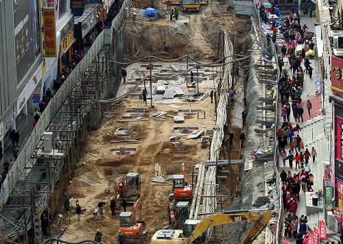 1月2日,逛街的市民穿过德化街工地一侧的临时通道。近日,郑州市德化街地下人防工程全面开工。据了解,该工程在规划时引入地下空间建设理念,集地下人防、地铁通道、综合配套三大功能于一体,建成后将极大地缓解市中心商业区人车混行、交通拥堵现状,提升核心商业圈的集聚功能,增强郑州城市防护能力。位于郑州市中心二七塔商业圈的德化街于1905年建成,与大同路、福寿街一起成为郑州市最为悠久的商业街道。新华社记者 王颂 摄