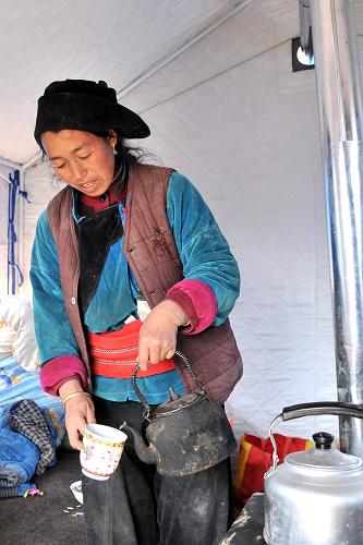 2月12日,受灾村民包王加村在黑多村的临时安置点里煮奶茶。新华社记者 陈斌 摄