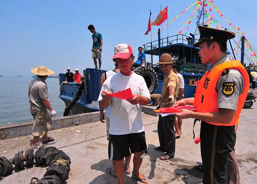 8月1日,在中国四大渔港之一的福建省石狮市祥芝渔港码头,福建石狮边防大队官兵把宣传材料送到出海渔民手中。新华社记者 魏培全 摄