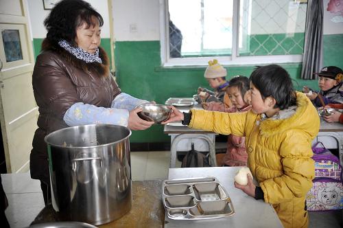 2月17日,在宁夏回族自治区隆德县凤岭乡冯碑小学二年级的教室内,一位学生正在从老师手中接过饭菜。新华社记者 彭昭之 摄