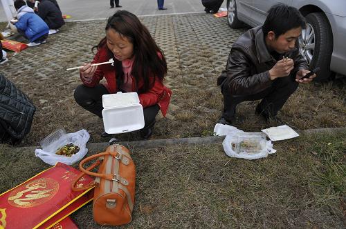 1月29日,陈顺付(右)和妻子在路边吃盒饭,准备转乘客车回家。新华社记者 欧东衢 摄