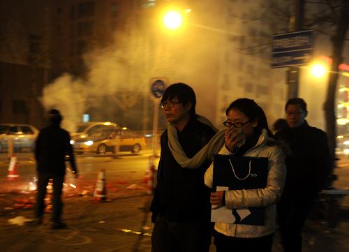 2月24日晚,北京东三环一小区外,一名行人用围巾捂住口鼻,以躲避路旁燃放烟花产生的烟雾。新华社记者 罗晓光 摄