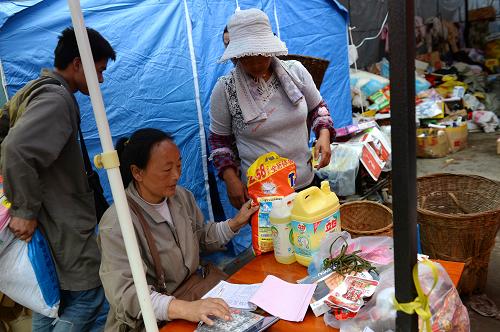 5月3日,村民用代金券在胡国香(中)开设的“爱心接力超市”结账。“胡国香是芦山龙门乡一个开着名为‘晶晶超市’的48岁的妇女,灾后却默默地做出了温暖众人心窝的举动,她把超市的食品和生活用品从废墟中扒出来,全部免费供给30多户120多位乡邻享用。”这个灾区的感人故事,经过新华社报道后,引起广大爱心人士的关注。在西藏务工的200多名四川农民工捐款20余万元,开设“爱心接力超市”——购买胡大姐的部分剩余物资发放给受灾群众,将这份灾区的大爱延续下去。开设“爱心接力超市”之后,胡国香给受灾群众免费发放代金券,受灾群众可在一定时期内在“爱心接力超市”选择各自需要的物资,以满足不同需求、避免救灾物资同类平均发放的浪费。目前,代金券已回收10万元左右。新华社记者 金良快 摄