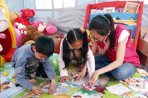 5月3日,志愿者在芦山县临时搭建的“儿童欢乐驿站”与当地儿童一起做拼图游戏。新华社记者 李明放 摄