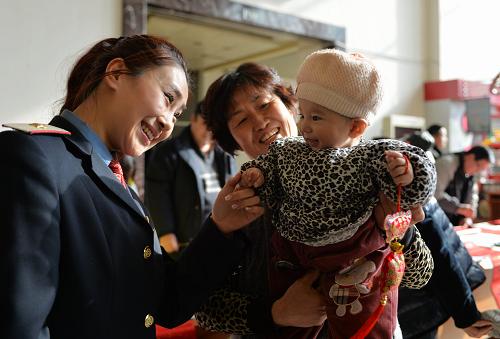 1月27日,兰州火车站客运员高子钦(左)向一位候车小朋友赠送年俗挂饰。新华社记者 陈斌 摄