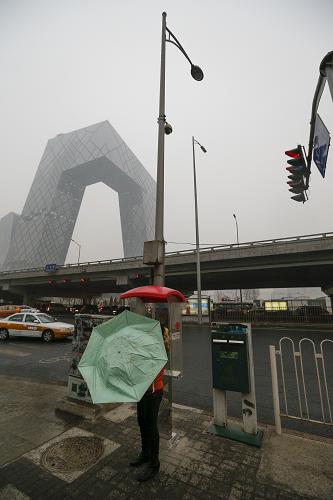2月26日,在被雾霾笼罩的央视新址大楼附近,一名行人撑起雨伞挡雨。新华社记者 沈伯韩 摄