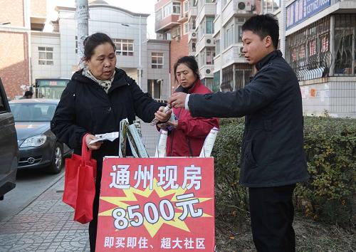 一名中介在北京通州区张家湾镇一小区内向过往行人介绍附近的小产权房。虽然其广告牌上写着每平方米只要“8500元”,但经询问,这是前不久的价,目前已经至少要1万元一平方米了(11月21日摄)。新华社记者 罗晓光 摄