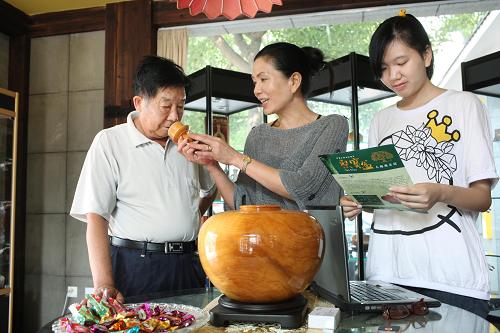 6月21日,店主陈金卿(中)请顾客(左)品鉴台湾木雕工艺品——桧木聚宝盆。新华社发(丁焕新 摄)