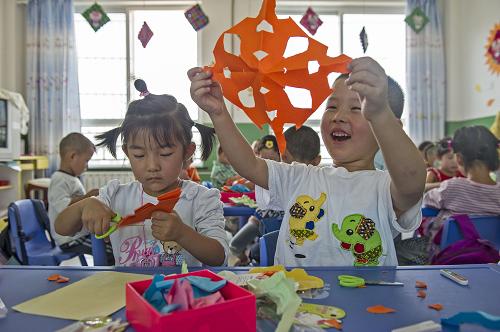 8月24日,幼儿园大一班孩子吕宸逸(右)向同学们展示自己的剪纸作品。新华社记者 陈诚 摄