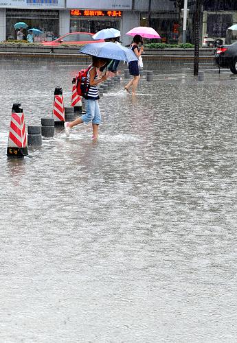 7月12日,南京新街口,市民冒雨趟过一处积水的道路。近日,江苏省出现大范围连续性强降雨,省气象台发布暴雨警报,并称未来几天强降雨仍将持续,提醒有关部门防范降雨可能造成的各种灾害。新华社记者 孙参 摄
