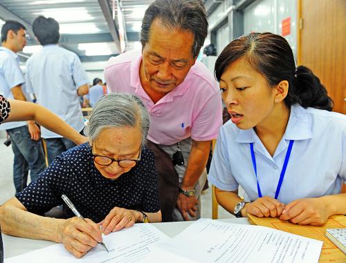 上海黄浦区露香园路地块92岁居民俞仁娣(前左)在房屋征收协议上签字(2012年6月30日摄)。新华社发(郭长耀 摄)