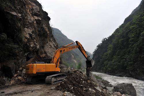 4月21日,在通往宝兴县的210省道上,一台大型挖掘机在清理公路路面上的碎石堆。新华社社记者刘潺摄