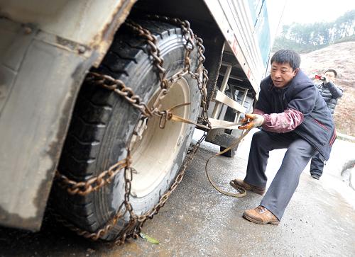 1月6日,在广西桂林市资源县资源镇通往湖南的资梅公路上,一名男子在给汽车装上防滑链,准备通过结冰道路。新华社记者 陆波岸 摄