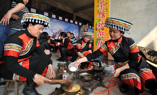 3月7日,在广西桂林市恭城瑶族自治县,当地妇女在打油茶准备招待客人。广西桂林市恭城瑶族自治县各族同胞自古以来就有打油茶、喝油茶的习俗,恭城人每天早餐都要“打油茶”,有的家庭甚至三餐离不开油茶,喝油茶已成为他们饮食中不可缺少的一部分。恭城油茶制作特别讲究,必须有专门的制作工具,油茶的主要原料是茶叶和姜。制作时,先把适量茶叶放入碗中用开水浸泡5-10分钟,洗净倒于茶叶隔中滤干,加入生姜,也可放入花生米、大蒜米。然后将茶锅置于火炉上,往锅内放一点食用油,待茶锅烧烫,将备好的茶叶、生姜、花生米、大蒜米一起倒入茶锅中边炒边锤,锤炒至茶叶沾锅,有香气溢出时倒入开水,边倒开水边不断搅动,煮沸两三分钟后加入食盐,用茶叶隔把茶水分别滤入碗中,撒入葱花、香菜末,再加入米花、脆果、酥花生即可上桌食用。如今,恭城油茶不仅是当地各族同胞家居不可或缺的食品,还是他们招待贵客嘉宾的必需品,成了瑶乡民族饮食文化一道独特的风景线。