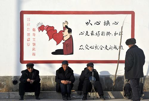 宁夏中卫市沙坡头区镇罗镇河沟村几名村民坐在村里的文化墙前晒太阳(1月31日摄)。新华社记者 彭昭之 摄