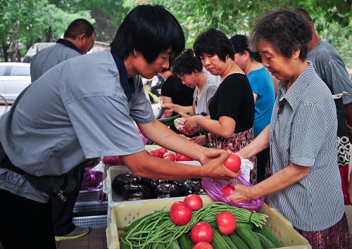 7月8日,蔬菜直销点服务人员(左)帮助社区居民选购新鲜蔬菜。新华社记者 张超群 摄