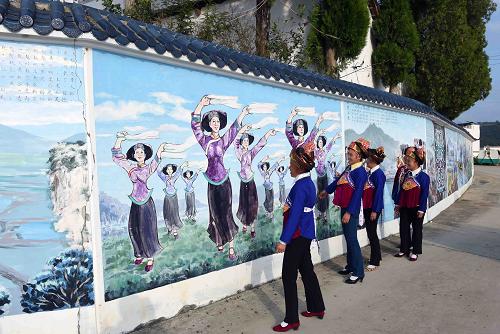 砚山县盘龙乡法土龙村的壮族妇女在观看围墙上的壮族风情画廊（12月10日摄）。