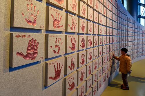 12月14日，在新馆“争取持久和平”展区，一位小观众在抗战老兵手印墙前参观。