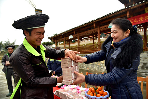 1月13日，广西环江毛南族自治县双乐苗寨柑橘种植大户韦玉荣（左）在领取分红款。当日，广西环江毛南族自治县思恩镇双乐苗寨举办年度分红大会，加入当地家文果业合作社的26户苗族同胞每户领到了5至15万元不等的分红款。果农参与专业合作社发展柑橘种植是环江县果业发展的一个缩影。近年来，当地在苗木培育、果树病虫害防治、果园现代化管理以及水果批发等领域拥有丰富经验的大型合作社面向环江乡村吸纳果农，带动果农集体脱贫致富。新华社发（高东风 摄）