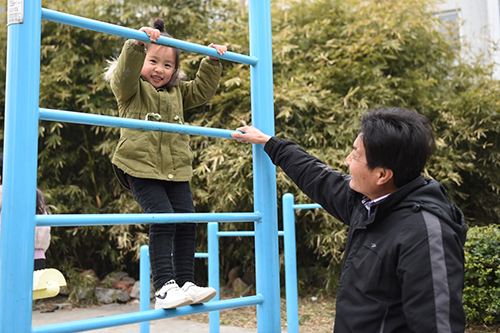 55岁的村民徐荣林（右）陪着孙女馨馨在渔民新村的健身休闲区玩耍（2月16日摄）。